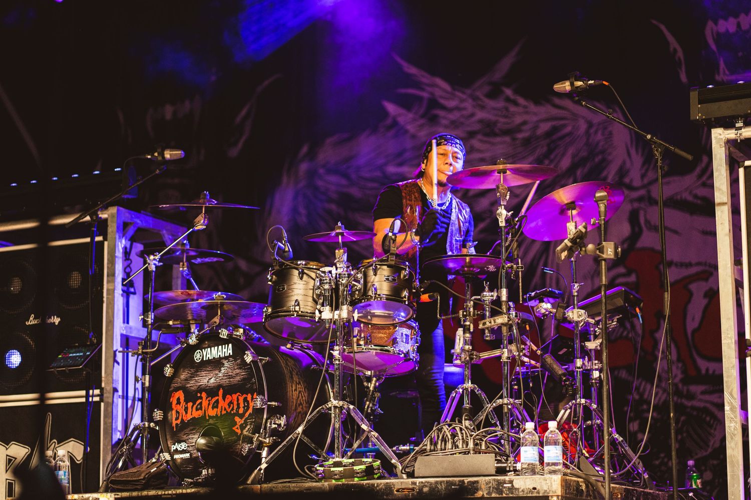 Dramatic concert stage setup with purple lighting illuminating an elaborate drum kit.