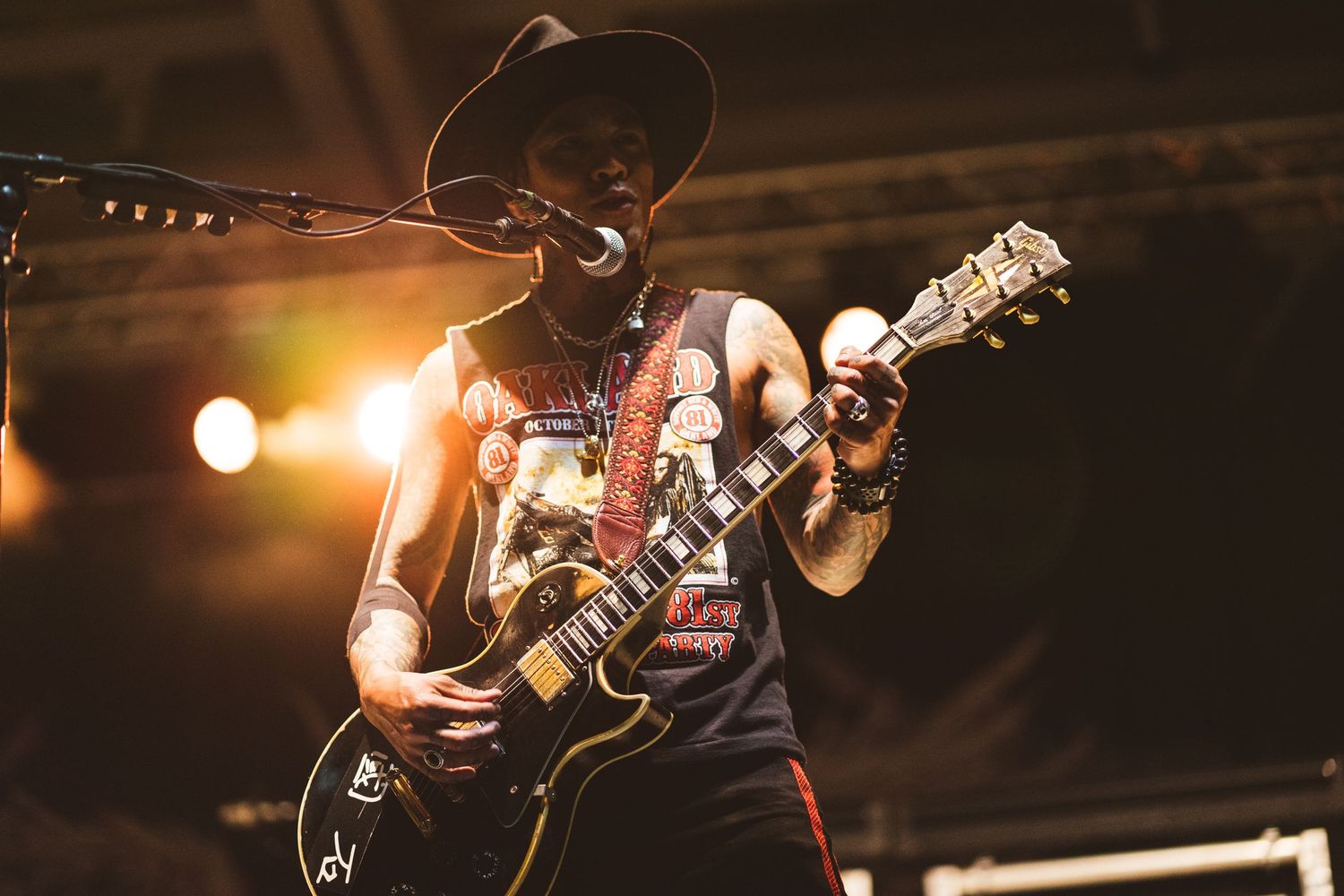 Performer in cowboy hat plays guitar under warm stage lighting during concert.