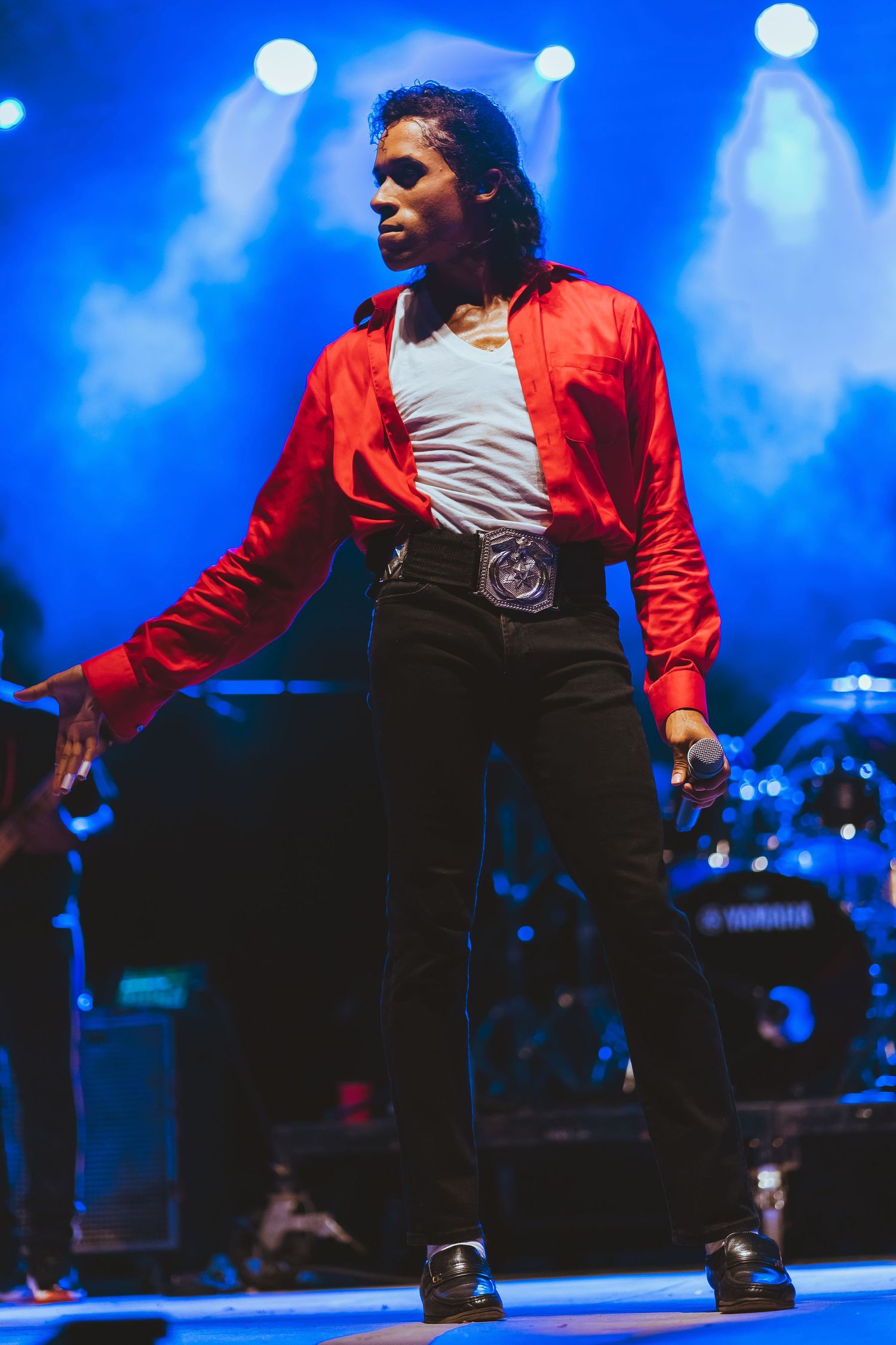 Energetic stage performance with dramatic blue lighting and red jacket costume.