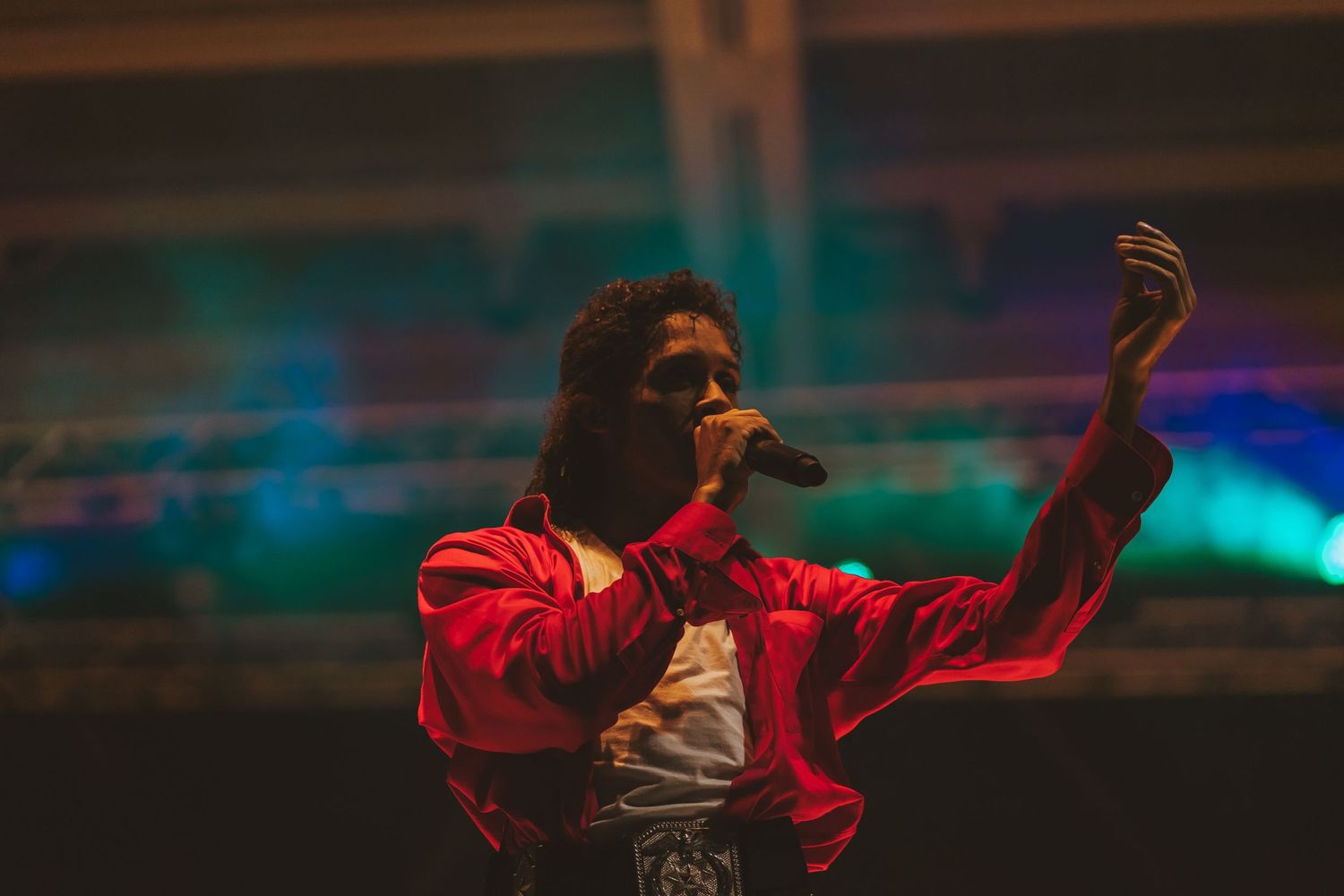 Dynamic concert performance with dramatic lighting and red jacket against blue background.