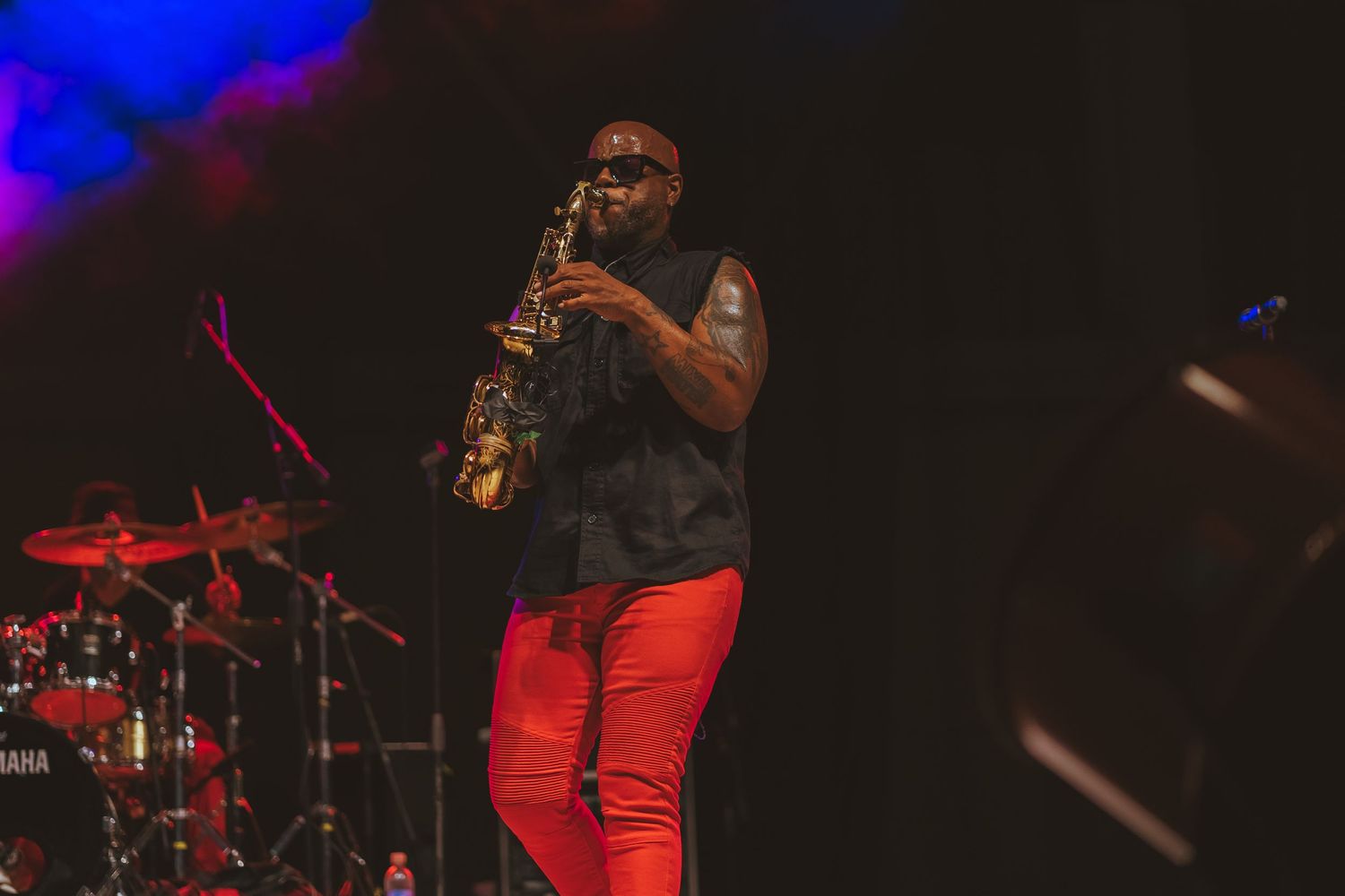 Saxophone player performs on dark stage with blue and red lighting effects.