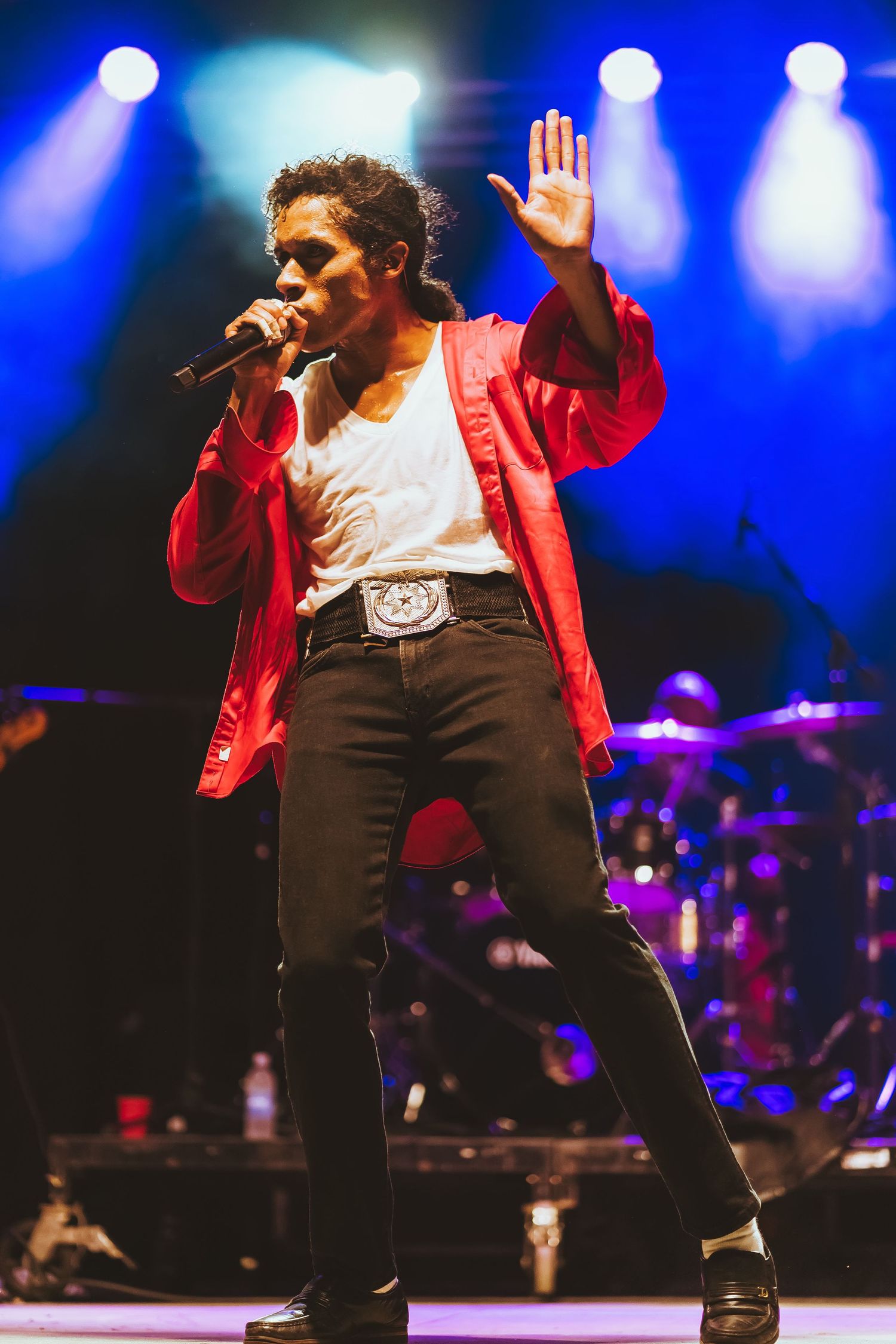 Dynamic stage performance with iconic red jacket and silver belt buckle under blue spotlights.