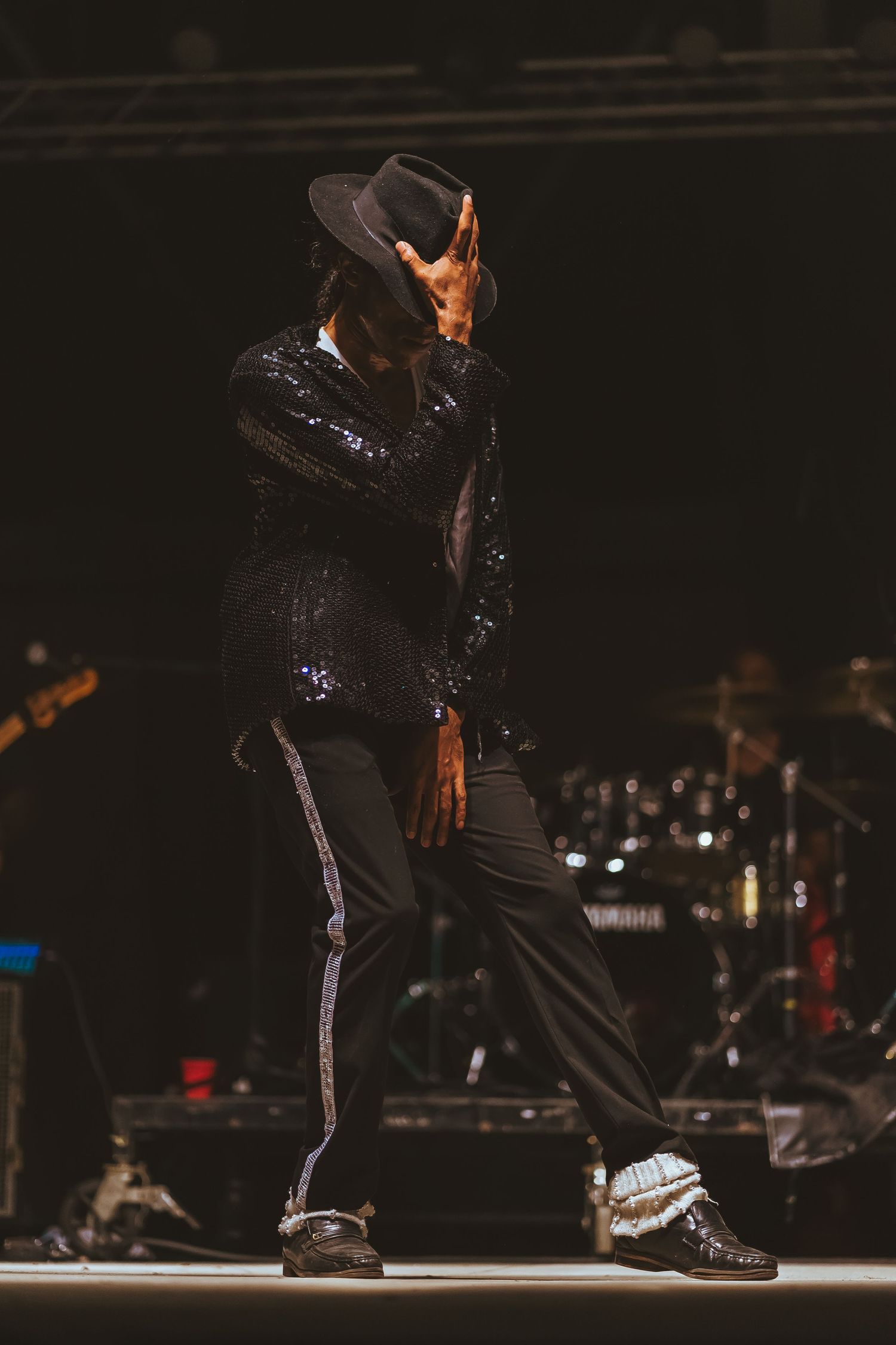 Performer in sparkly black outfit and hat strikes iconic dance pose on stage.