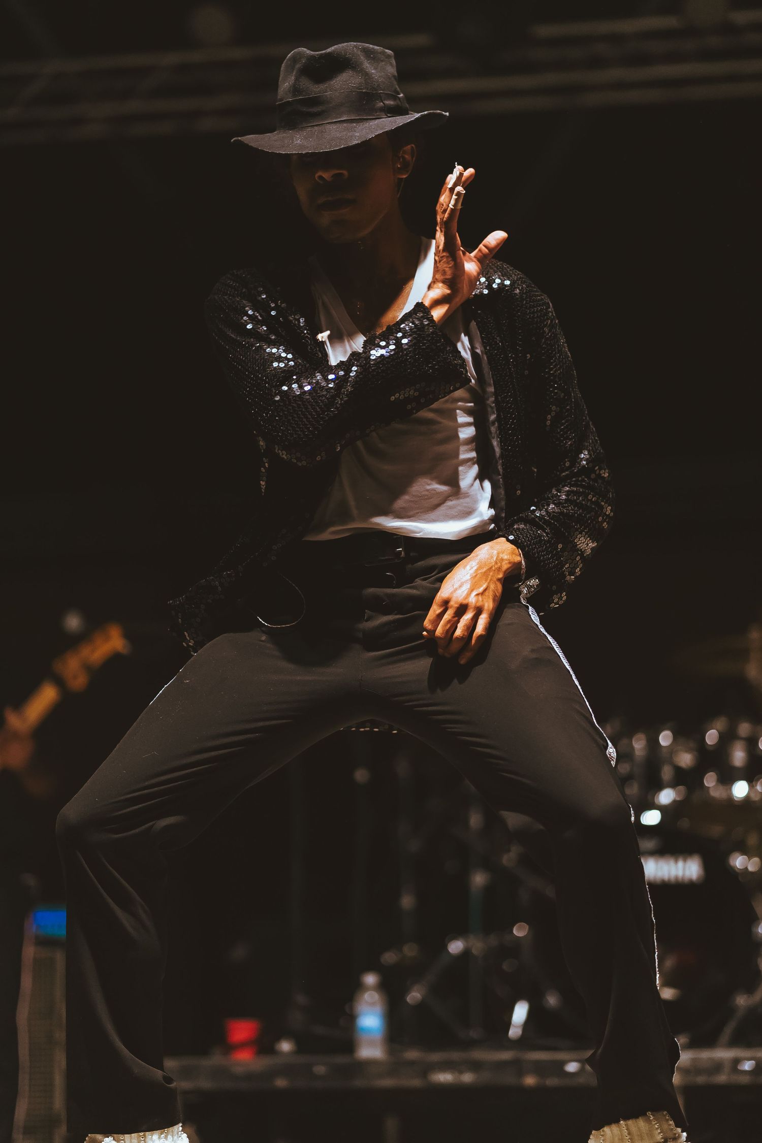 Dramatic stage performance in black hat and sparkly jacket with precise choreographed movements.