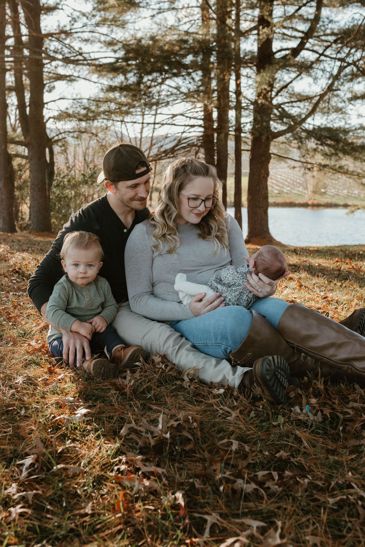 A family relaxes together on fallen autumn leaves under pine trees.