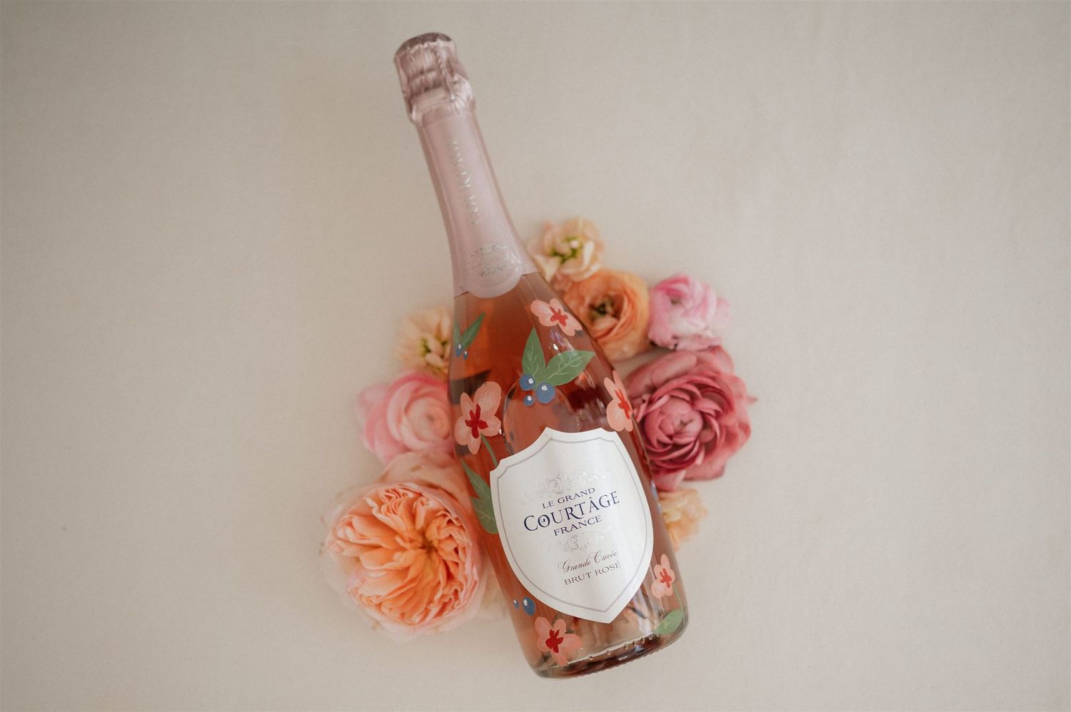 Pink champagne bottle decorated with fresh flowers against a neutral background.