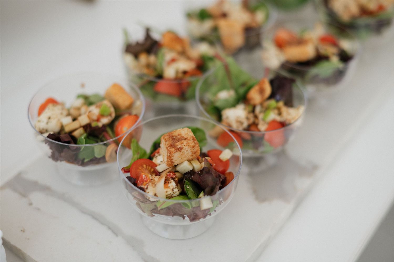 Individual appetizer portions of fresh salad with seafood served in small clear glass bowls on a white surface.