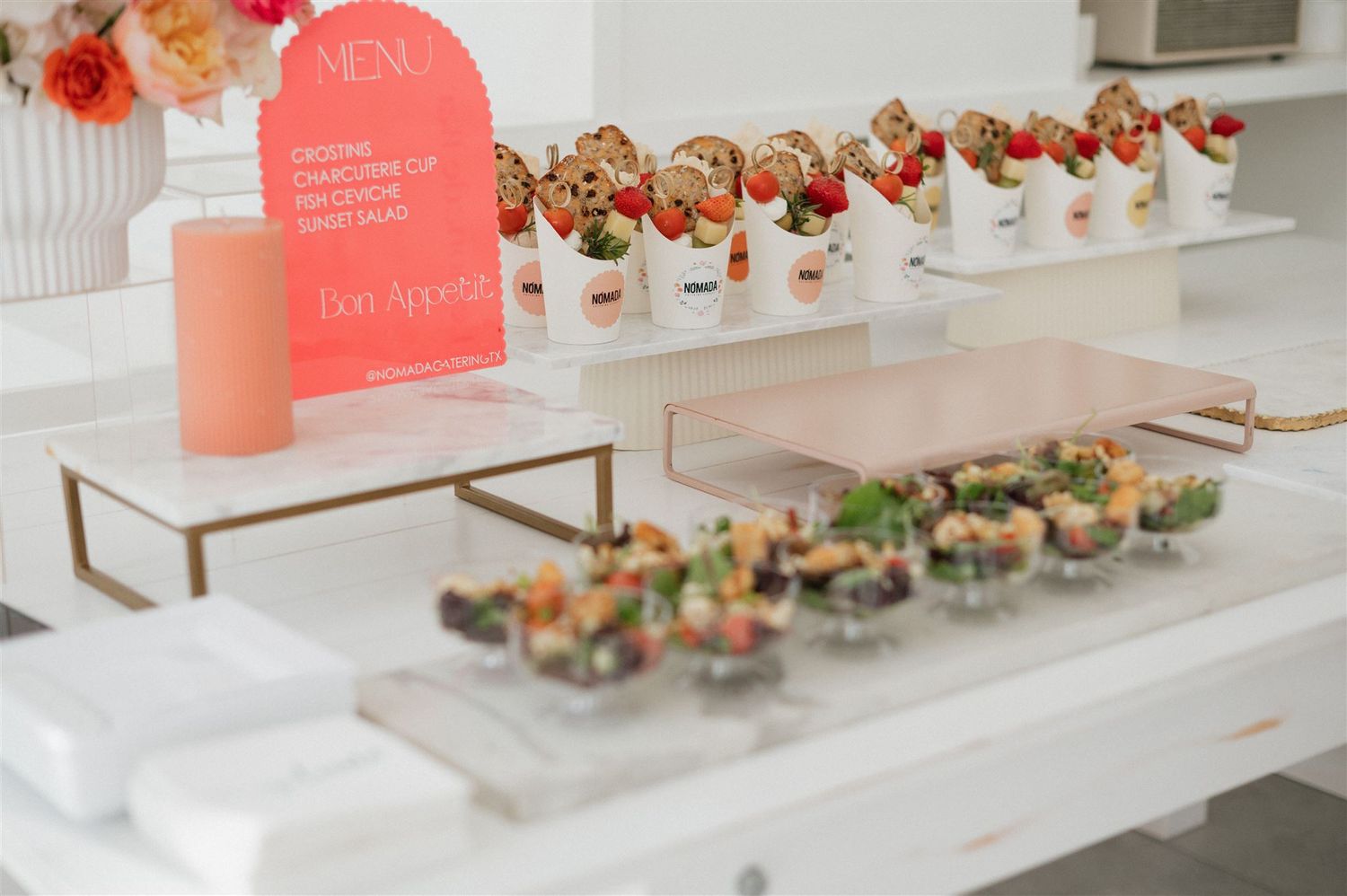 Elegant white event table display with rows of dessert cups and pink menu signage on marble stands.