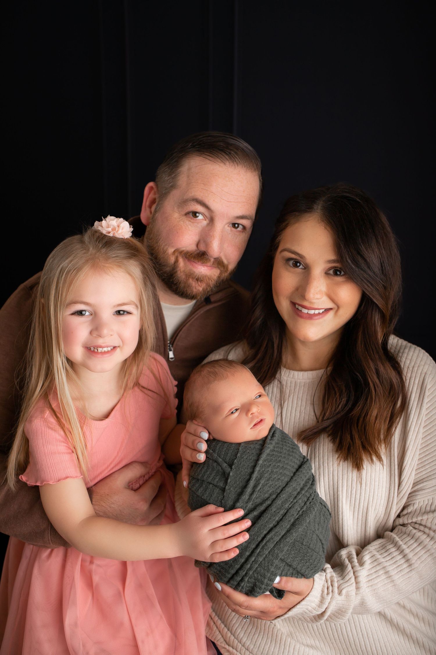 Studio portrait of family group against dark backdrop wearing coordinated neutral tones.