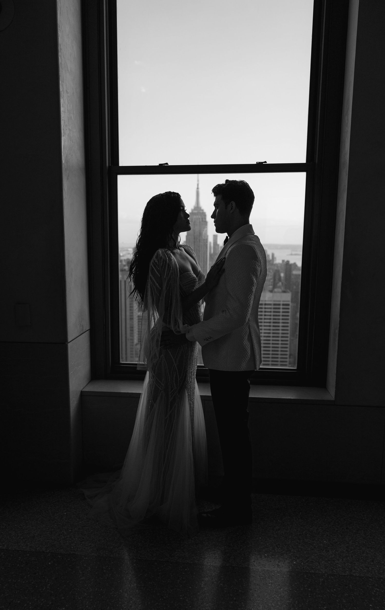 Silhouetted couple embracing by window with Manhattan skyline in background.