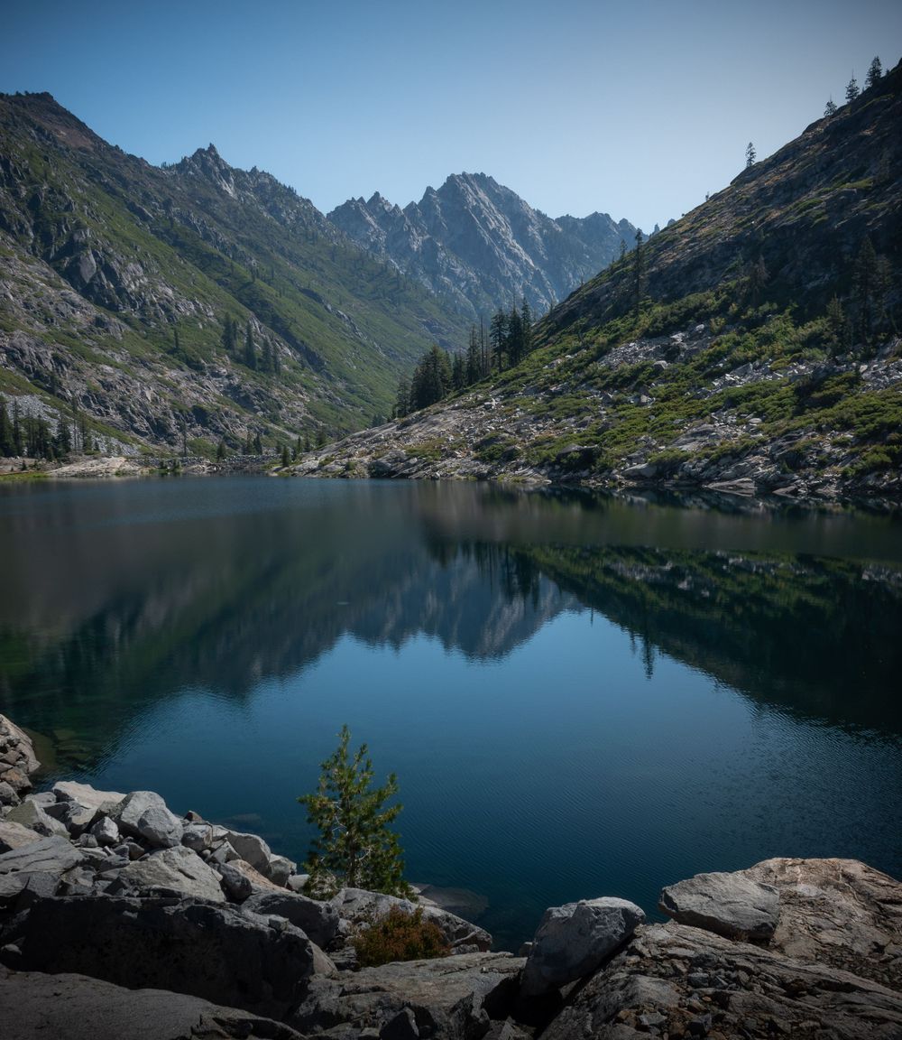 Serene alpine lake reflects surrounding mountain peaks and evergreen forest in pristine wilderness.