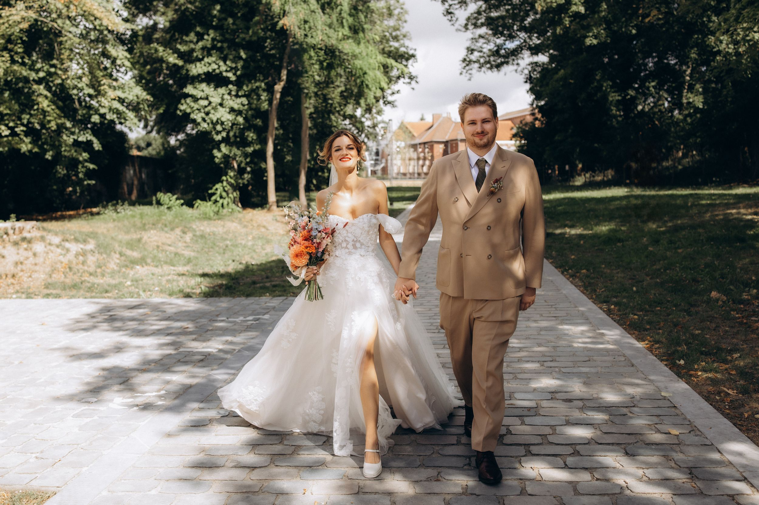 A couple in wedding attire walks together on a tree-lined path on their special day.