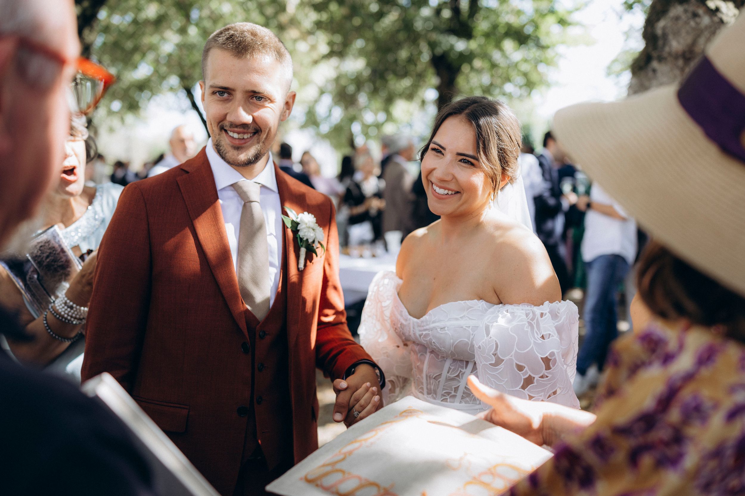 A happy couple at their outdoor wedding ceremony, with the bride wearing a white dress and groom in a brown suit.