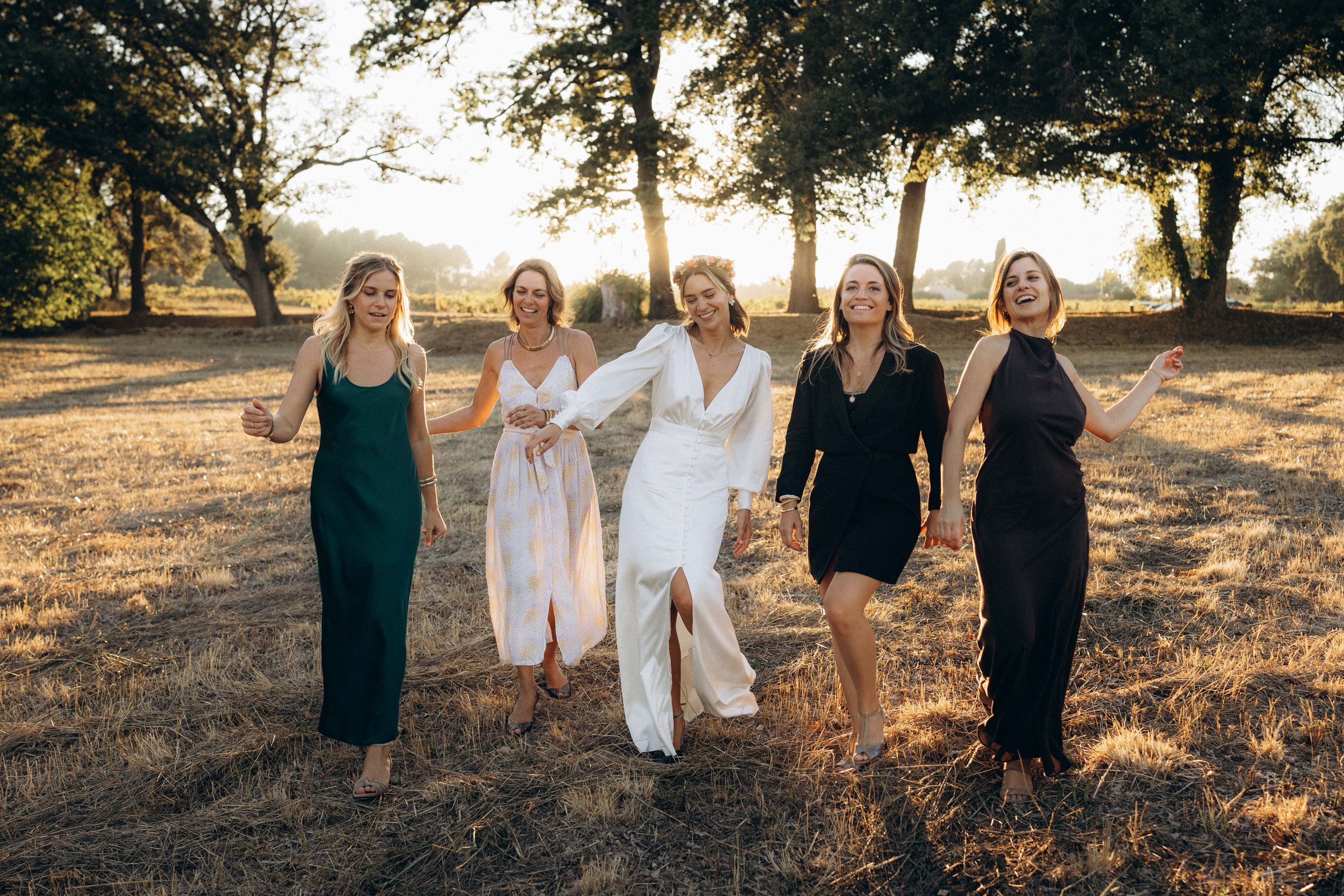 A group in black and white outfits poses together at sunset in a grassy field with trees in the background.