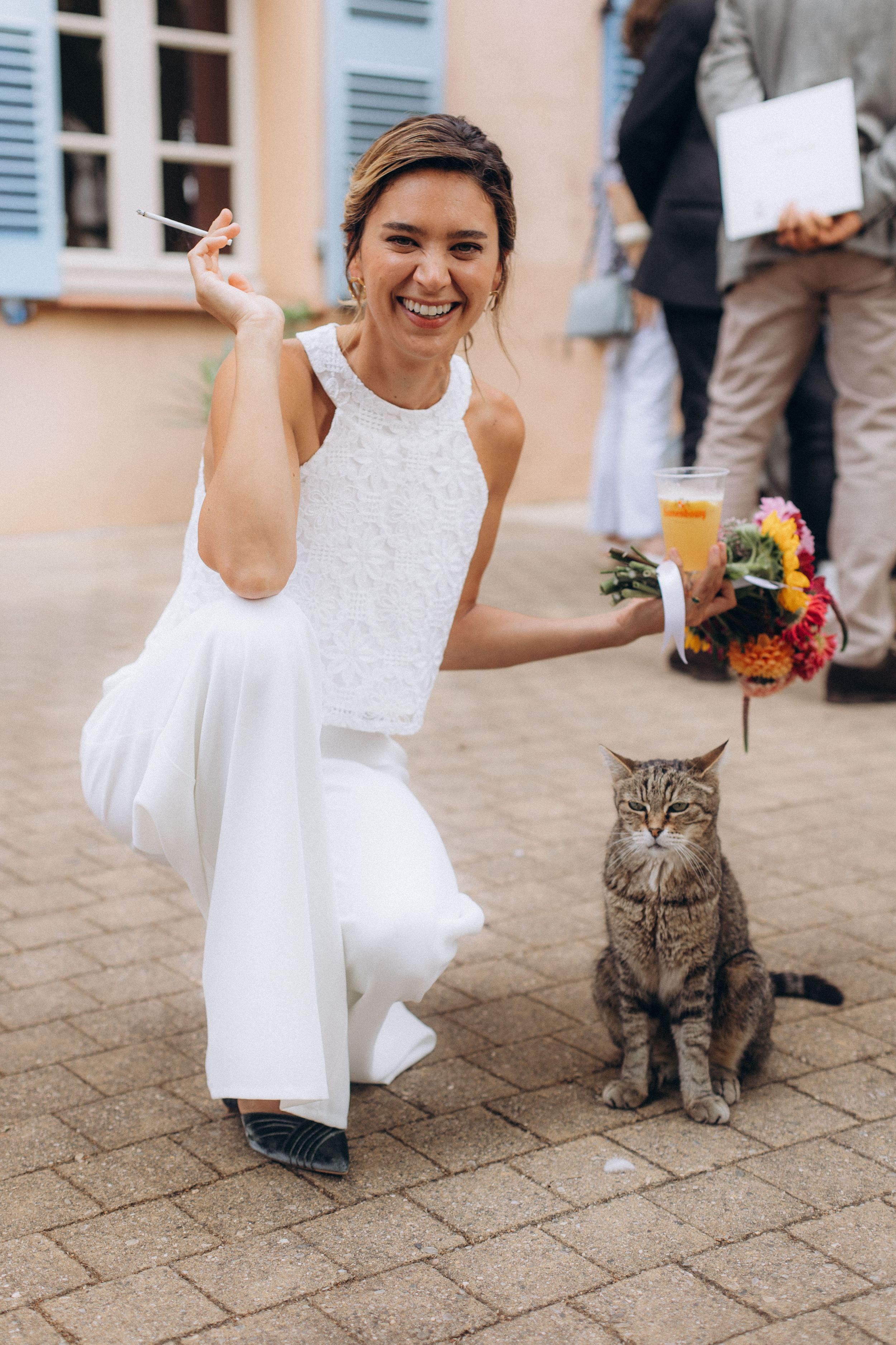 A sequence of photos showing someone in a white dress playfully interacting with a gray tabby cat on stone pavement.