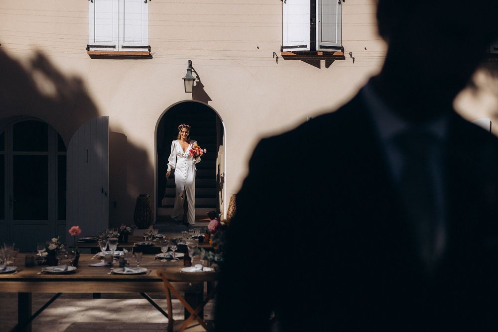 A wedding couple stands silhouetted in dramatic lighting against a white wall during their romantic celebration.