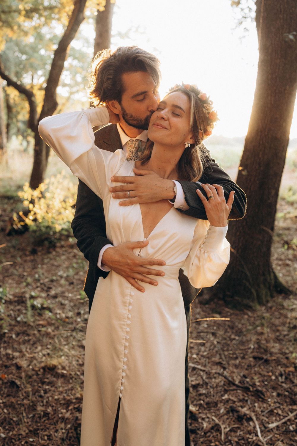 Romantic couple embraces in a sunlit forest setting wearing formal attire during intimate photo session.