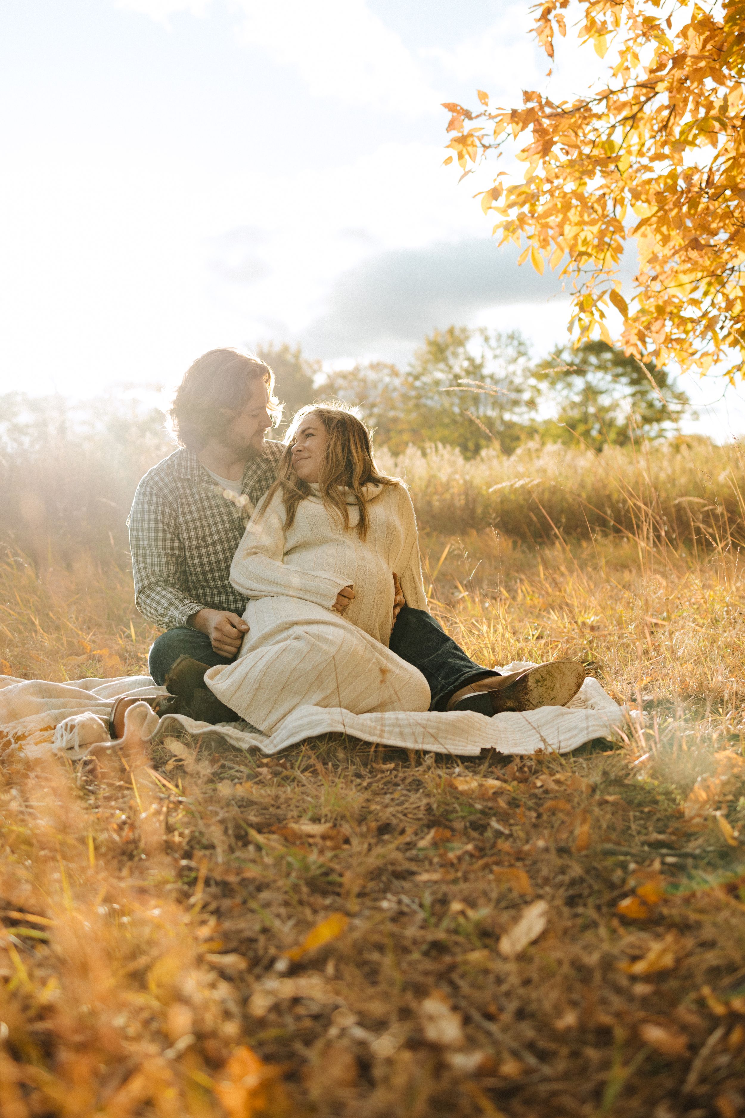 Couple having a tender moment while sitting on blanket in golden autumn field.