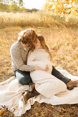 Intimate couple embracing on white blanket during autumn sunset photoshoot.