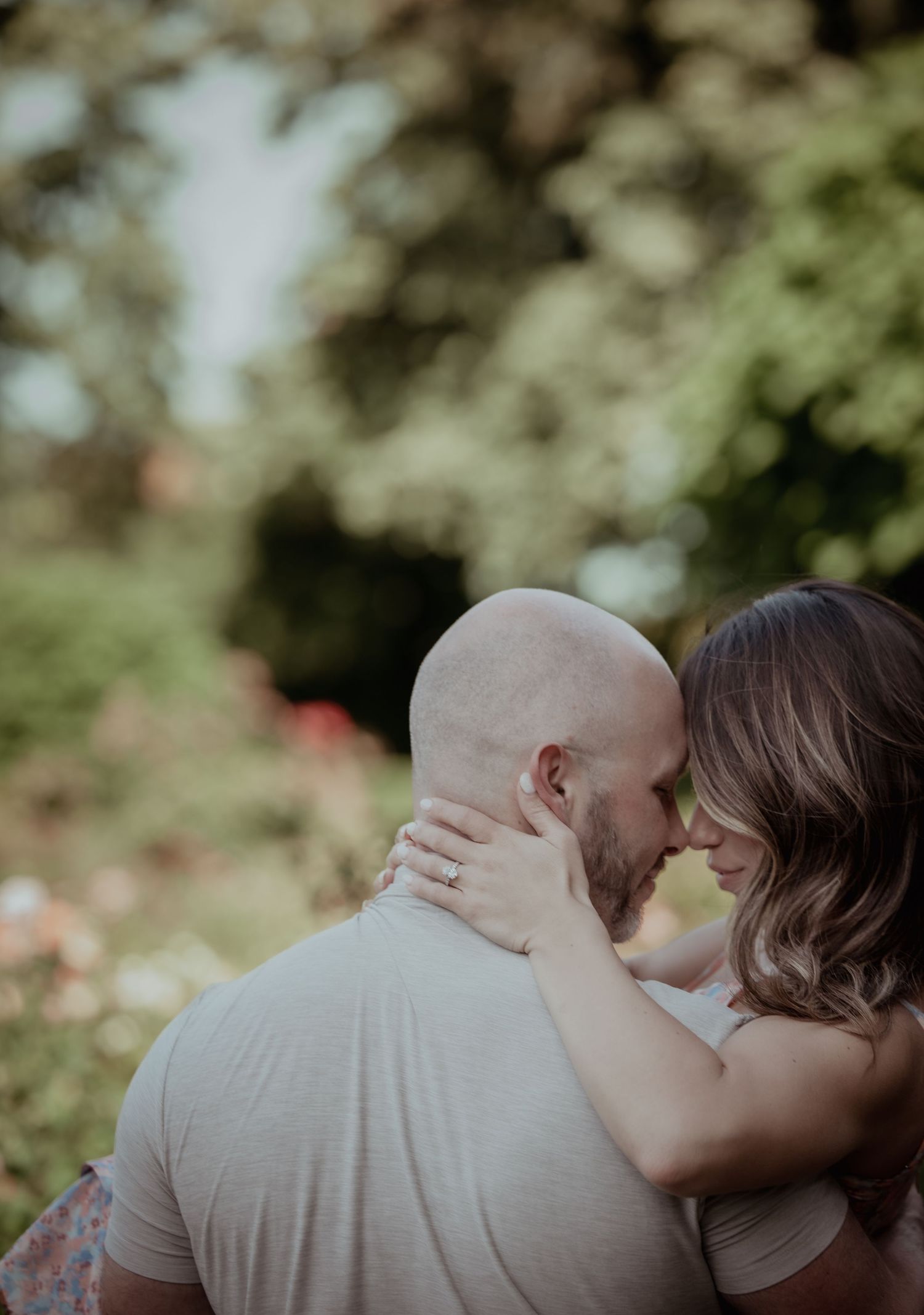 A romantic couple shares an intimate moment outdoors with soft natural lighting and greenery in the background.