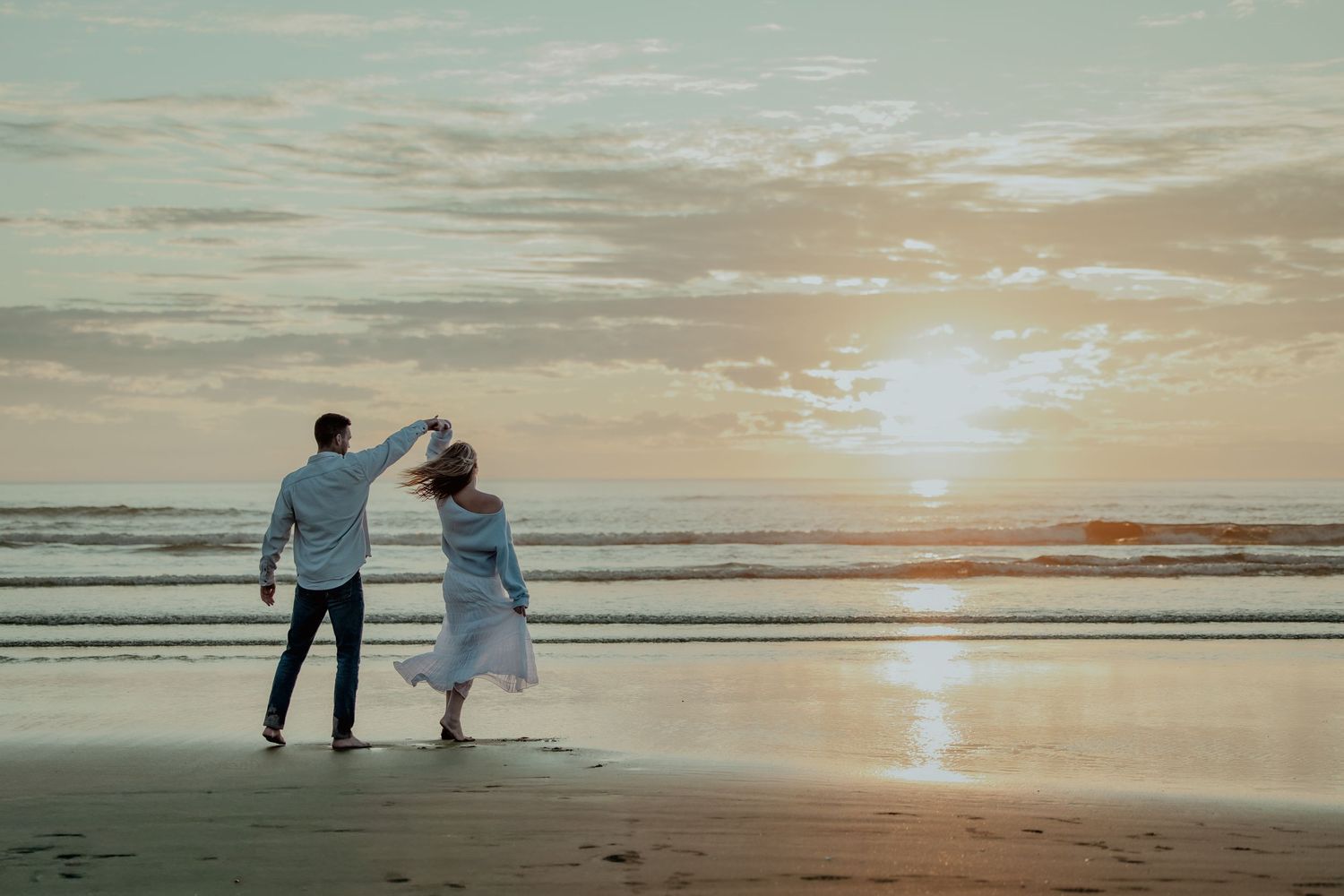 Couple walking along a misty beach at sunset with dramatic cliffs in the background.
