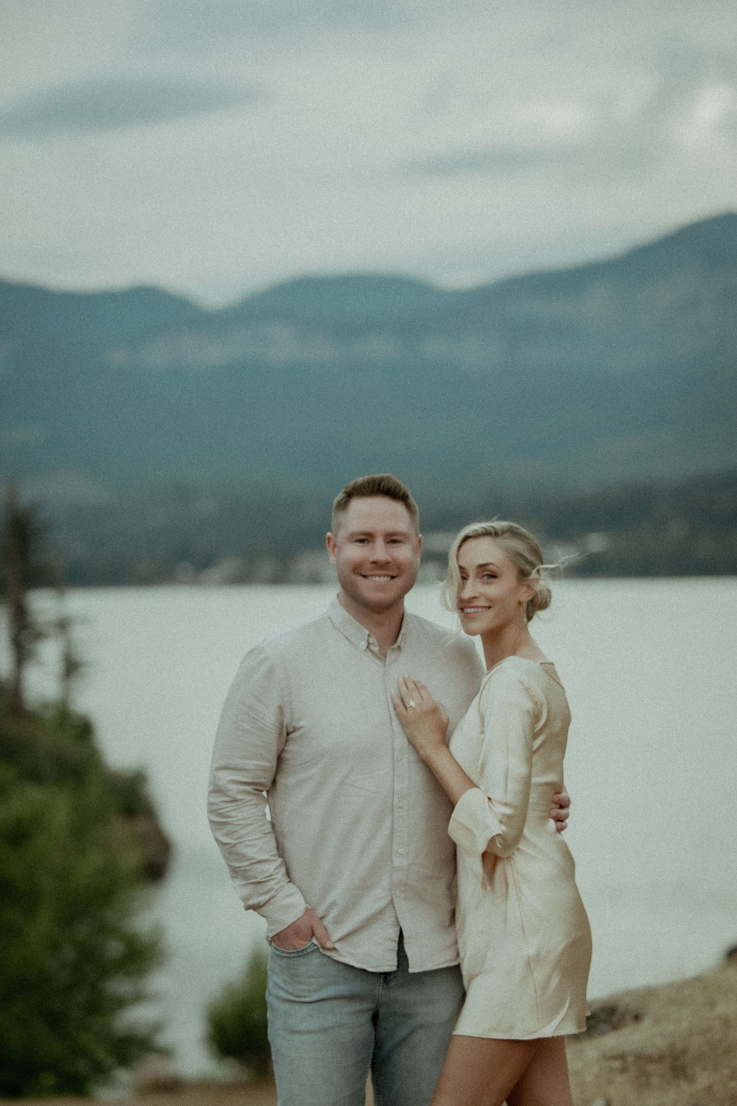 A couple poses together on a mountain overlook with a misty lake and mountains in the background.