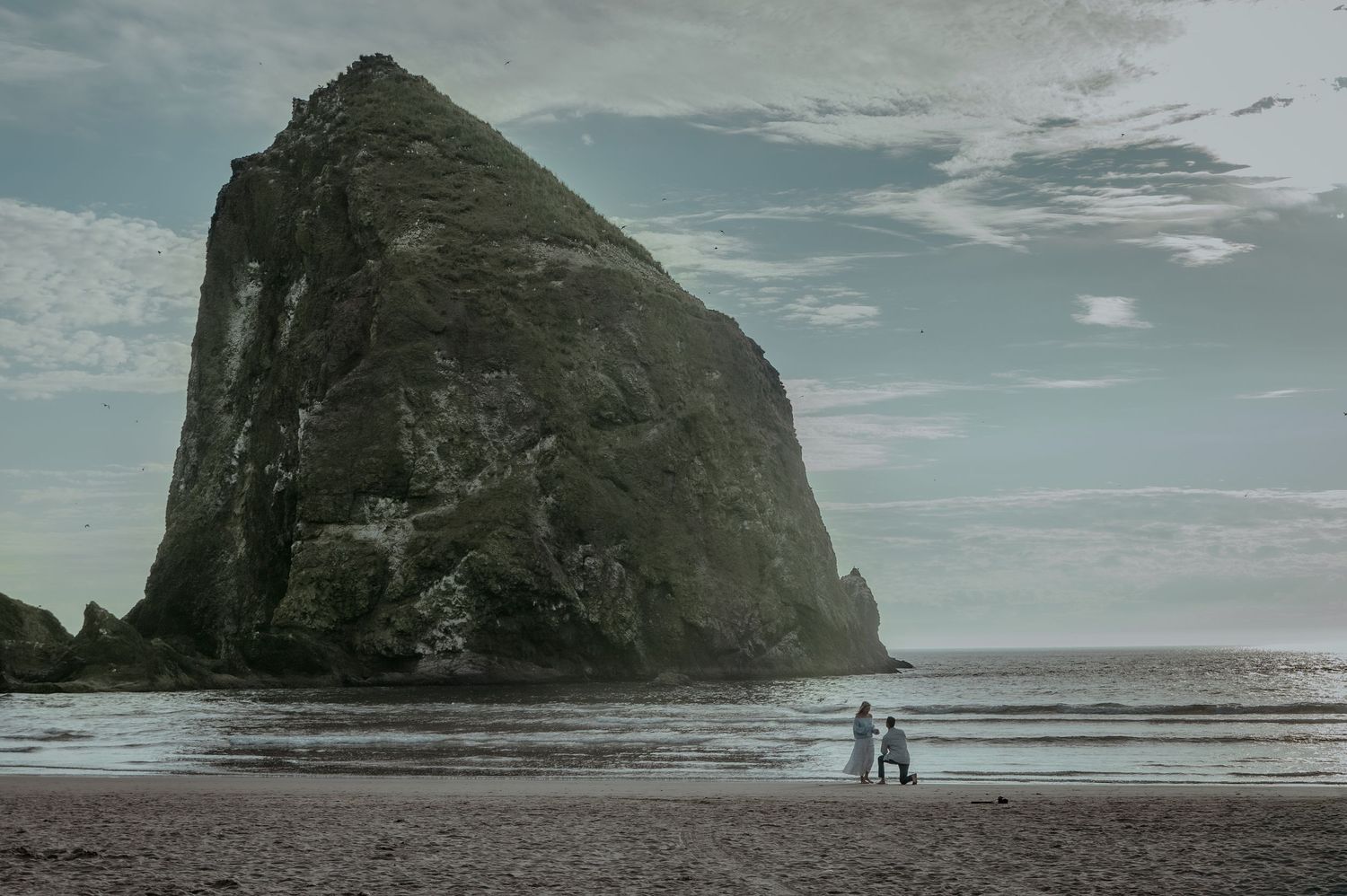Dramatic coastal landscape with large rocky cliffs and beach along the Pacific Ocean at sunset.
