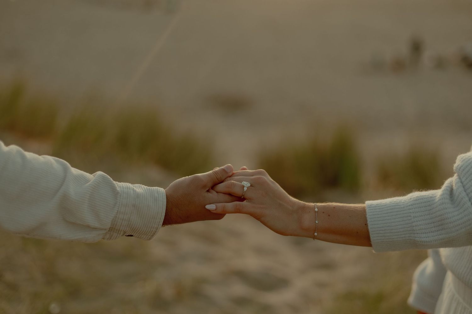 A close-up of two hands gently clasped together against a soft, blurred natural background.