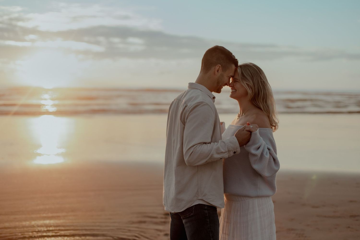 A romantic couple shares an intimate moment on the beach at sunset with golden light illuminating the scene.