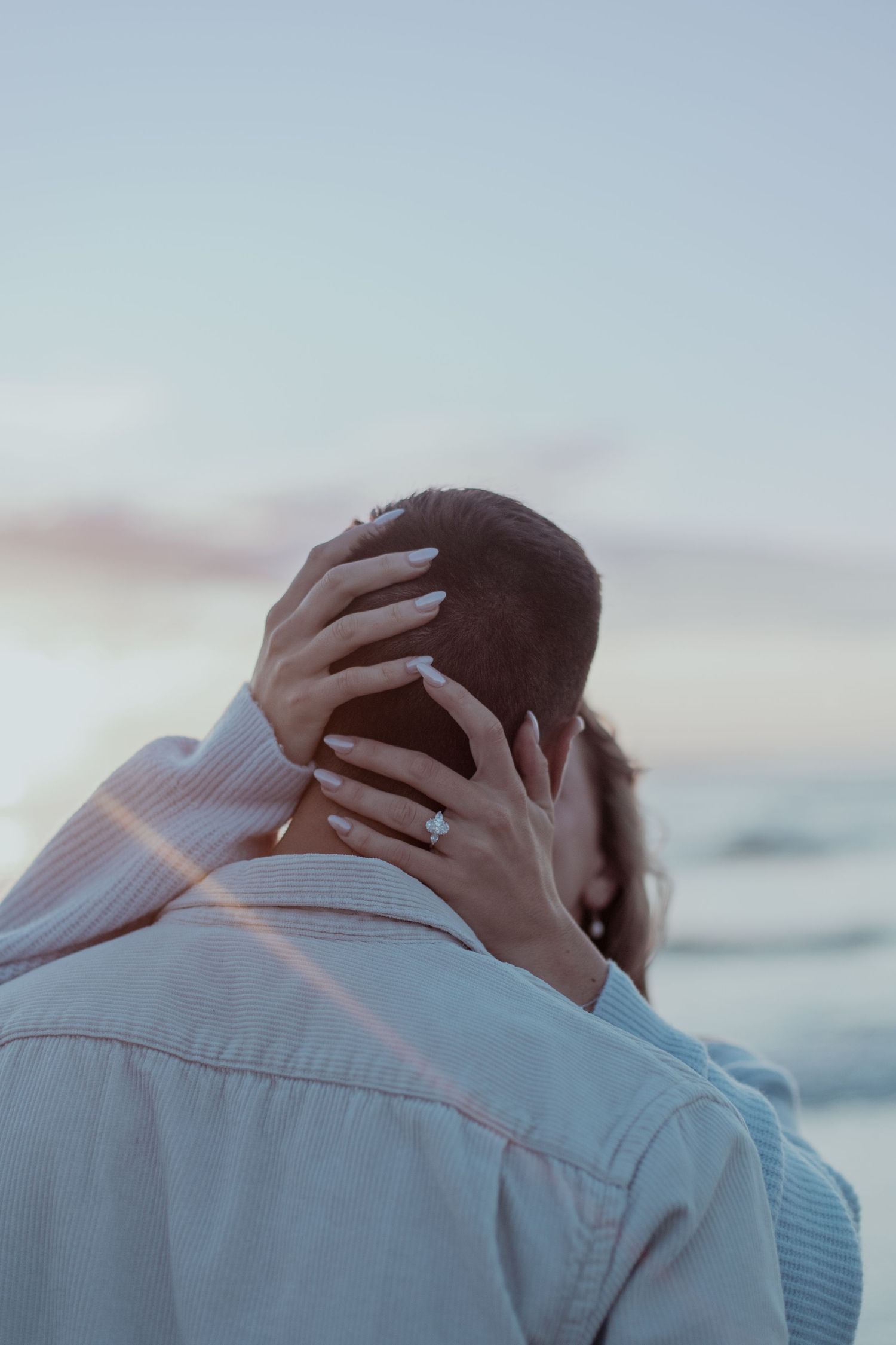 Person in light blue shirt holds their head while looking away against a cloudy sky background.