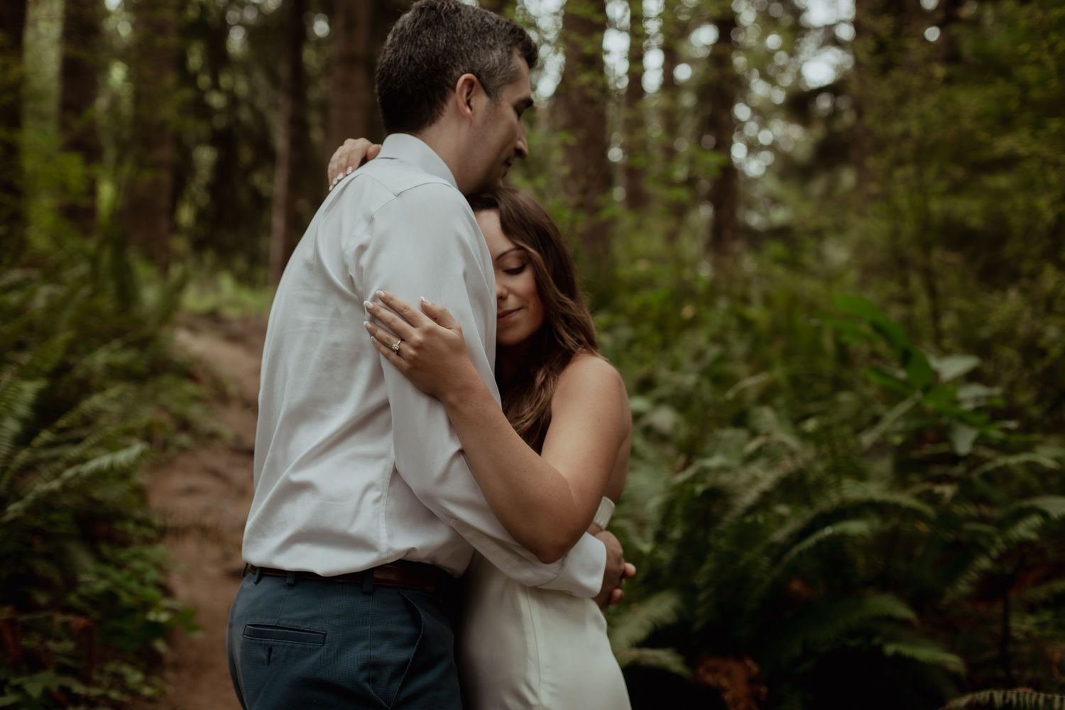 Couple embraces intimately in a lush green forest setting during an outdoor photo session.