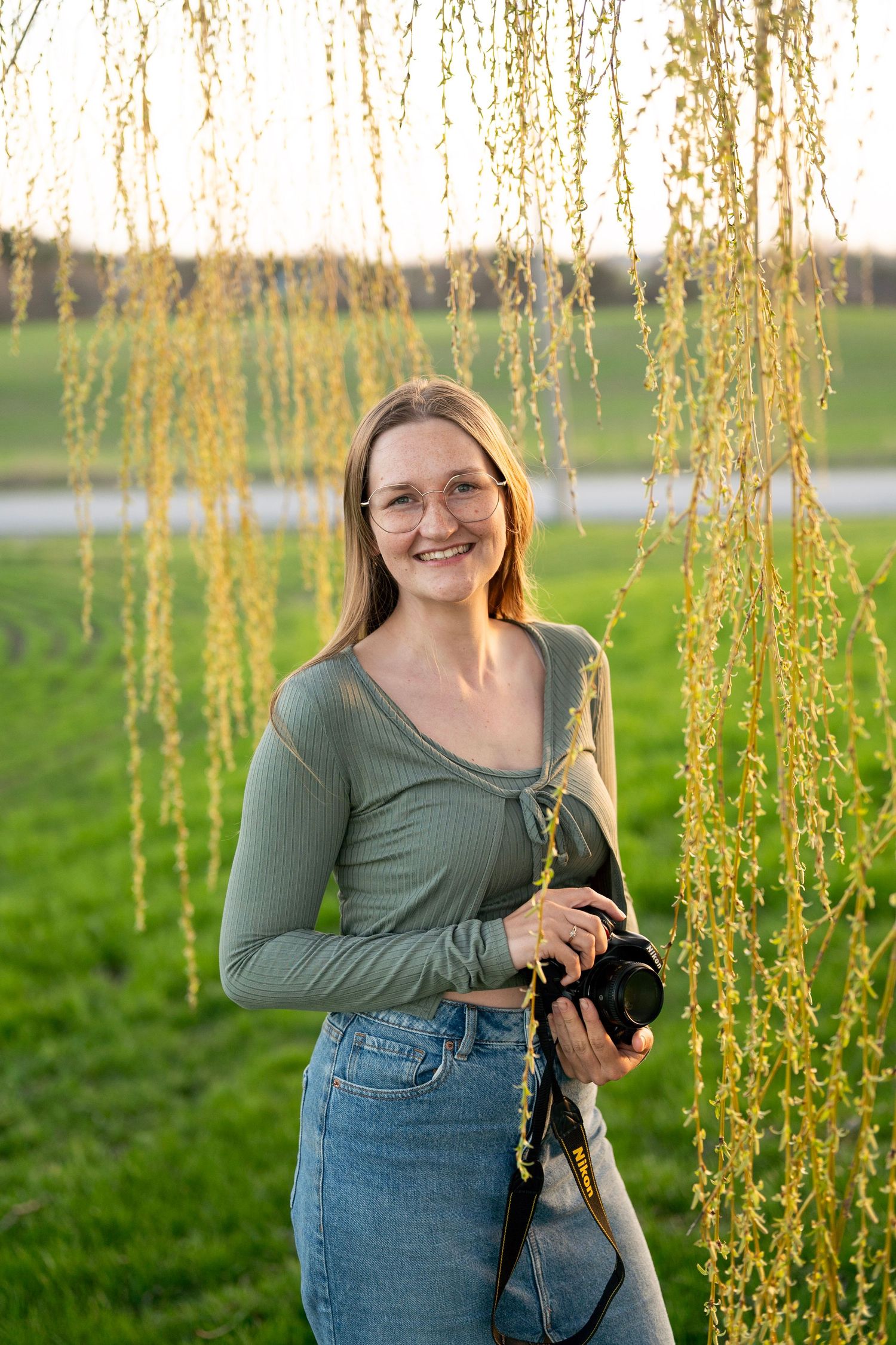 Portrait of photographer with camera during golden hour in summer park setting.
