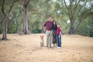 Family portrait with dog on dirt path surrounded by eucalyptus trees in natural outdoor setting.