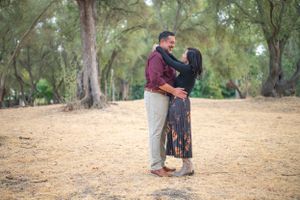 Couple embracing outdoors on autumn day with trees in background.