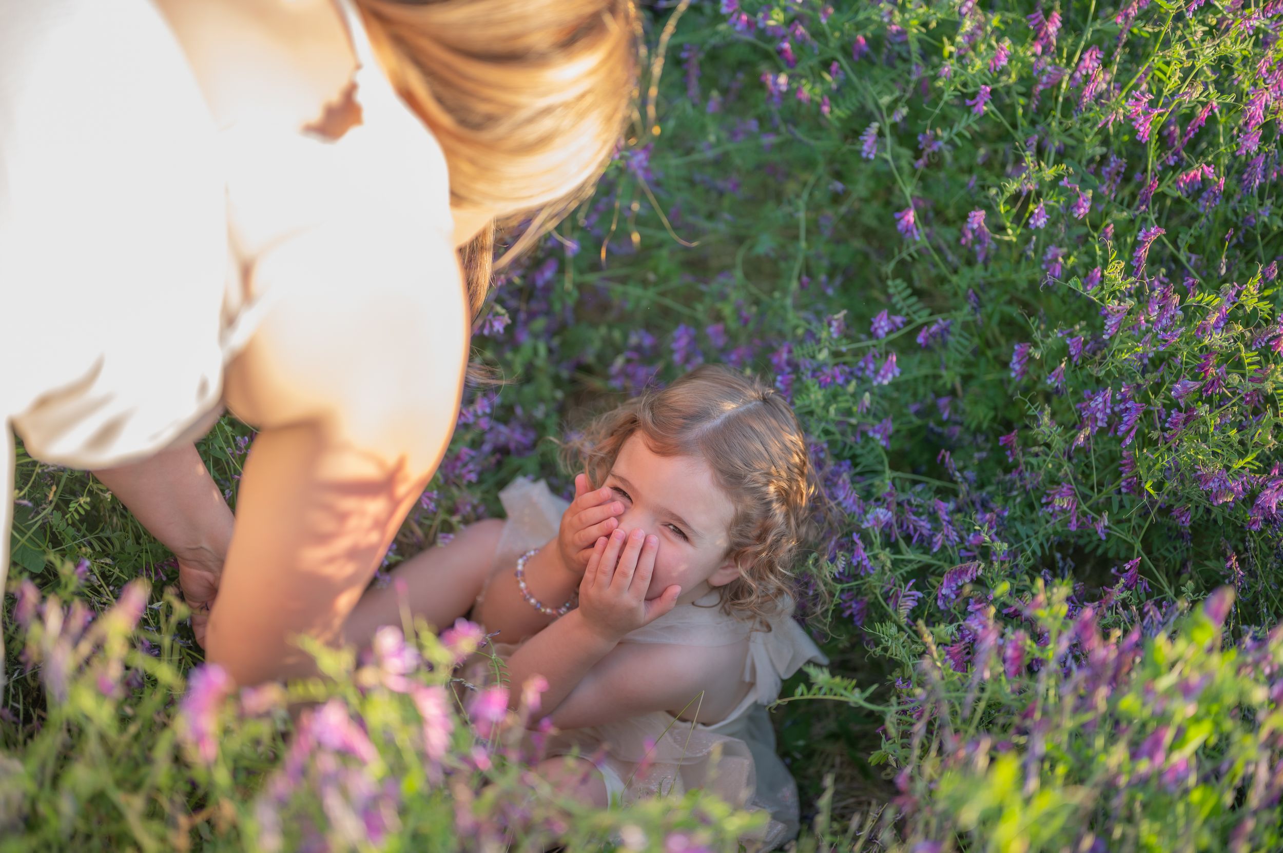 Child playing outdoors among vibrant purple wildflowers in a sunny garden setting during summer.