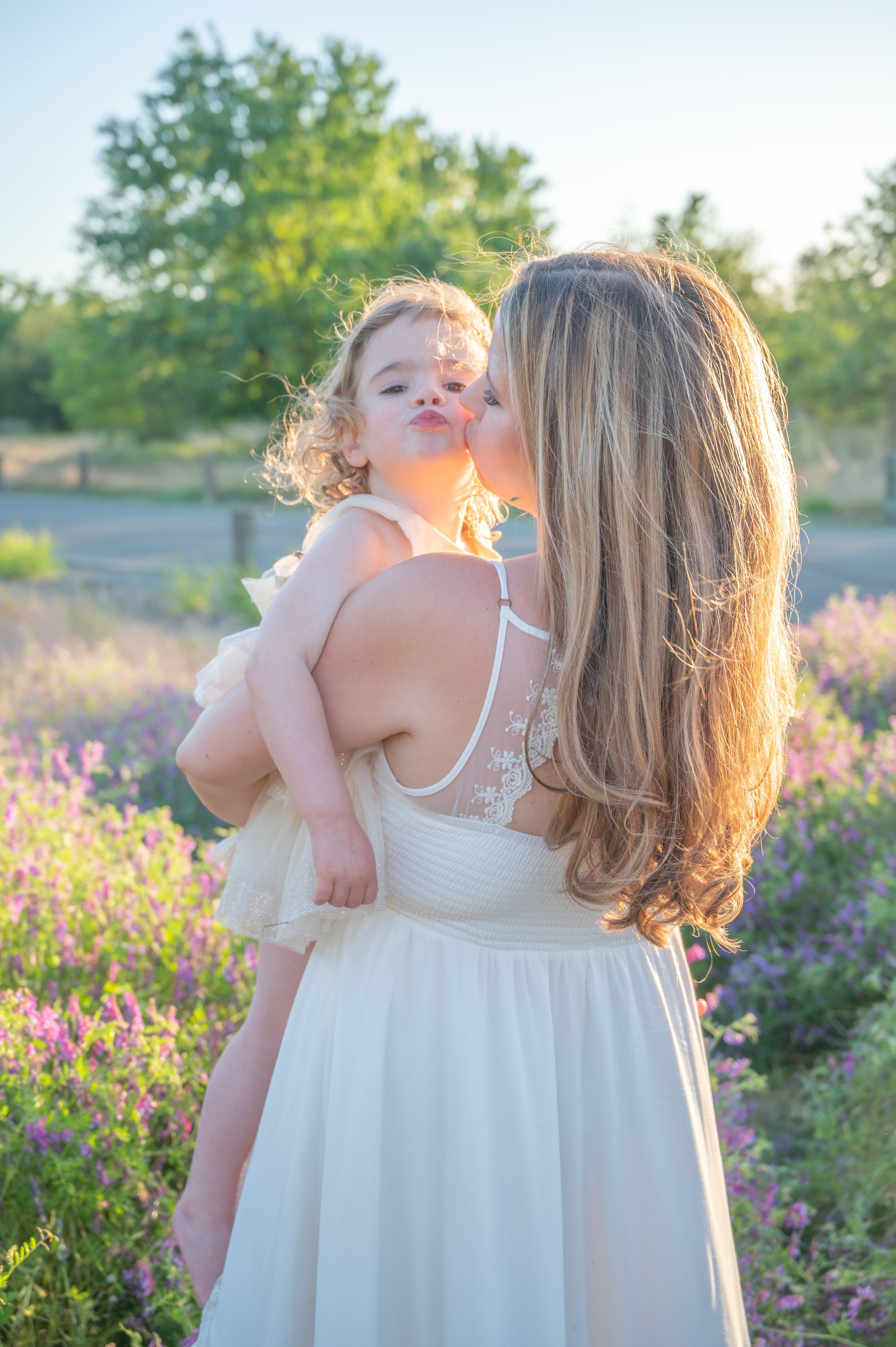 Woman in white dress with child embracing in a field of purple wildflowers at sunset.