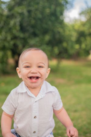 A happy toddler in a white button-up shirt laughing outdoors with a natural green background.