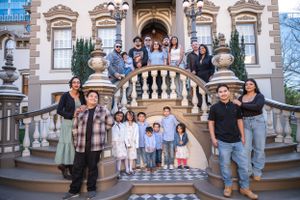 A large group gathers on the grand staircase of an ornate historic mansion with decorative architecture and stonework.