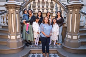 A group of people smile together while standing on ornate stairs with decorative pillars.