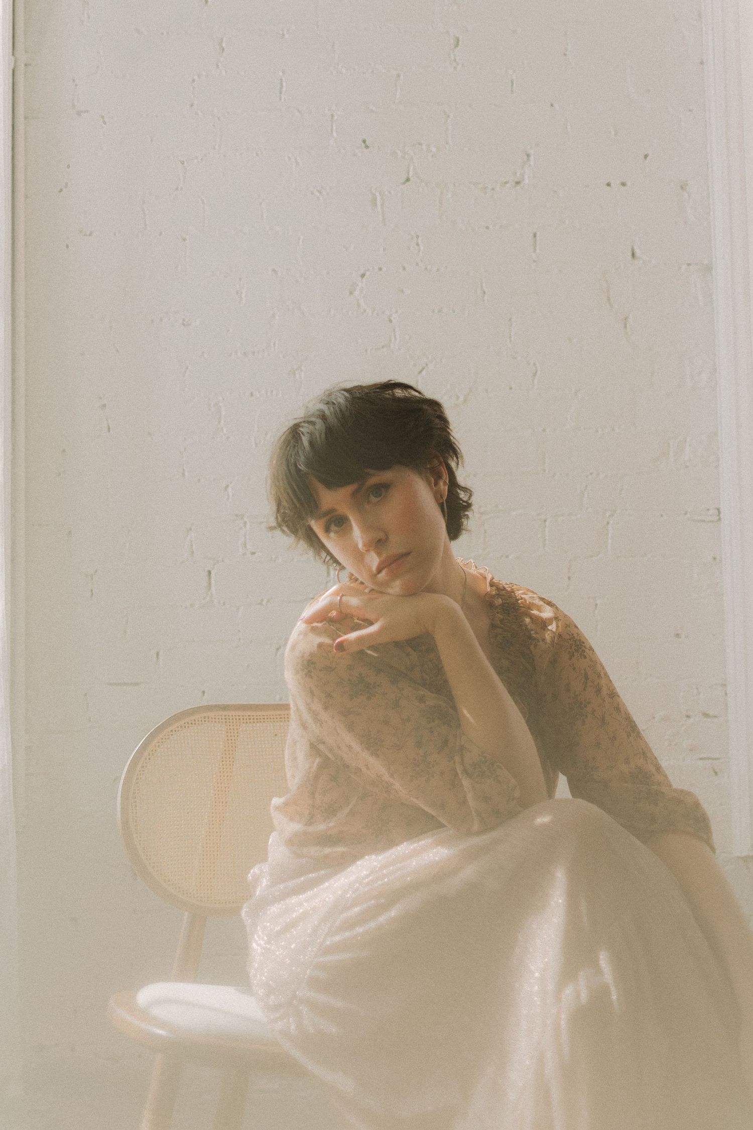 A dreamy portrait of someone in white lace posing thoughtfully on a chair.