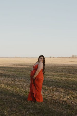 A person in a flowing red dress poses in a golden field at sunset against a clear sky.