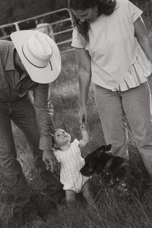 Black and white photo of a couple with a baby and dog on a farm, man wearing a cowboy hat.