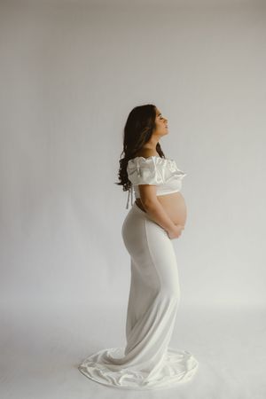 A series of minimalist maternity portraits showing a woman in a white dress against a light gray background.