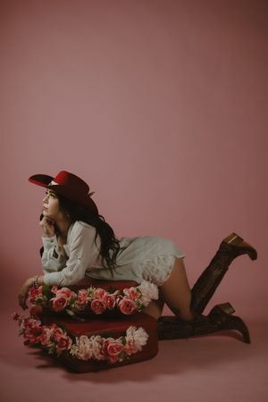 A figure reclines on a pink backdrop surrounded by pink and white roses in a romantic boudoir photo series.