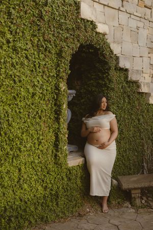 A series of connected photos showing someone in a cream dress posing against an ivy-covered stone wall.