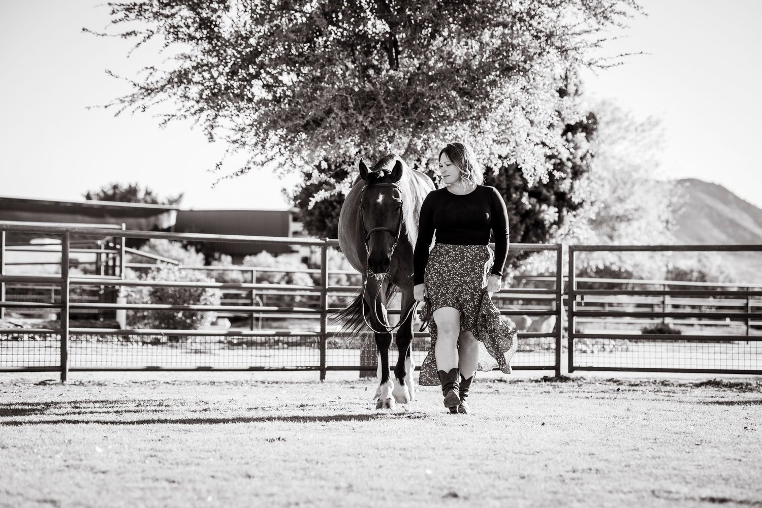 Black and white landscape photo of a rustic ranch with fencing and trees.