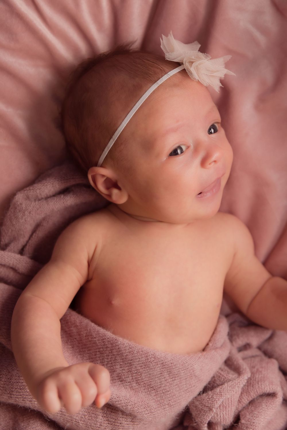 A smiling baby in a pink blanket looking up
