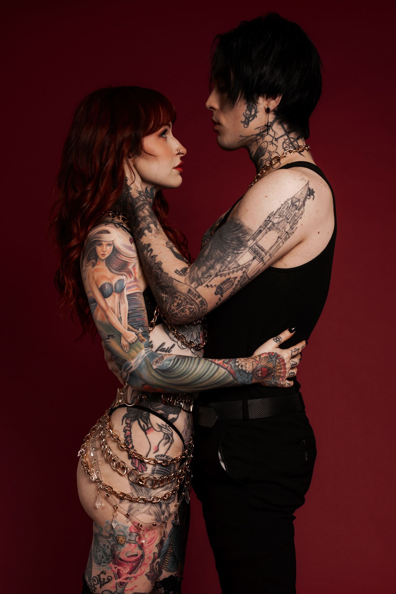 tattooed couple facing each other, with the woman touching the man’s face and the man holding her waist