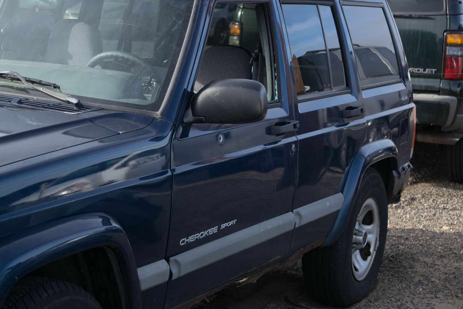 Side view of a dark blue Jeep Cherokee SUV parked on gravel.