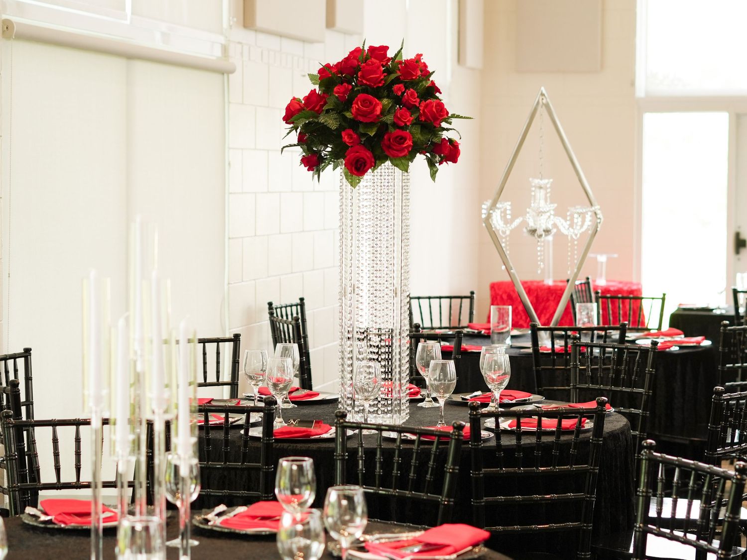Elegant wedding reception table with black chiavari chairs and tall crystal centerpiece with red roses.